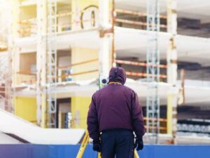 Construction surveyor using a total station to verify grid lines and floor elevations inside a multistory student housing project.